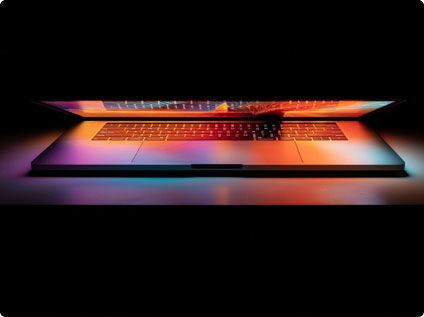 Pedego- A partially opened laptop emits colorful light from its screen, illuminating the keyboard and surrounding area against a dark background.