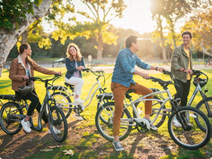 Pedego- Four people riding bicycles in a park, enjoying a sunny day with green trees in the background.